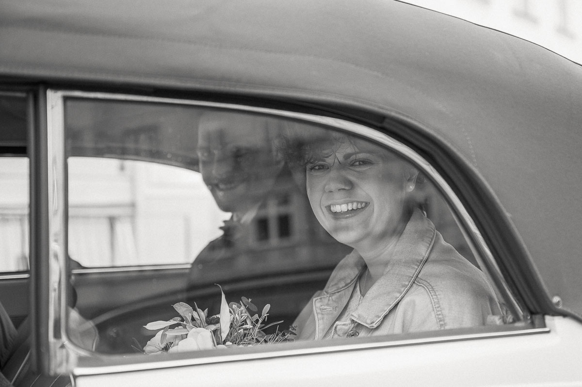 Braut sitzt lächelnd im Hochzeitsauto, fotografiert in einer dokumentarischen Schwarz-Weiß-Hochzeitsreportage.