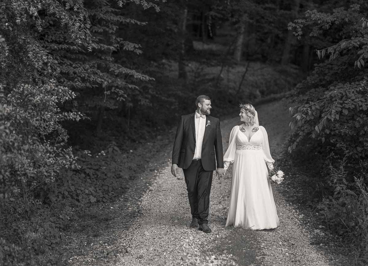 Brautpaar geht Hand in Hand einen Waldweg entlang, dokumentarische Hochzeitsfotografie in Schwarzweiß